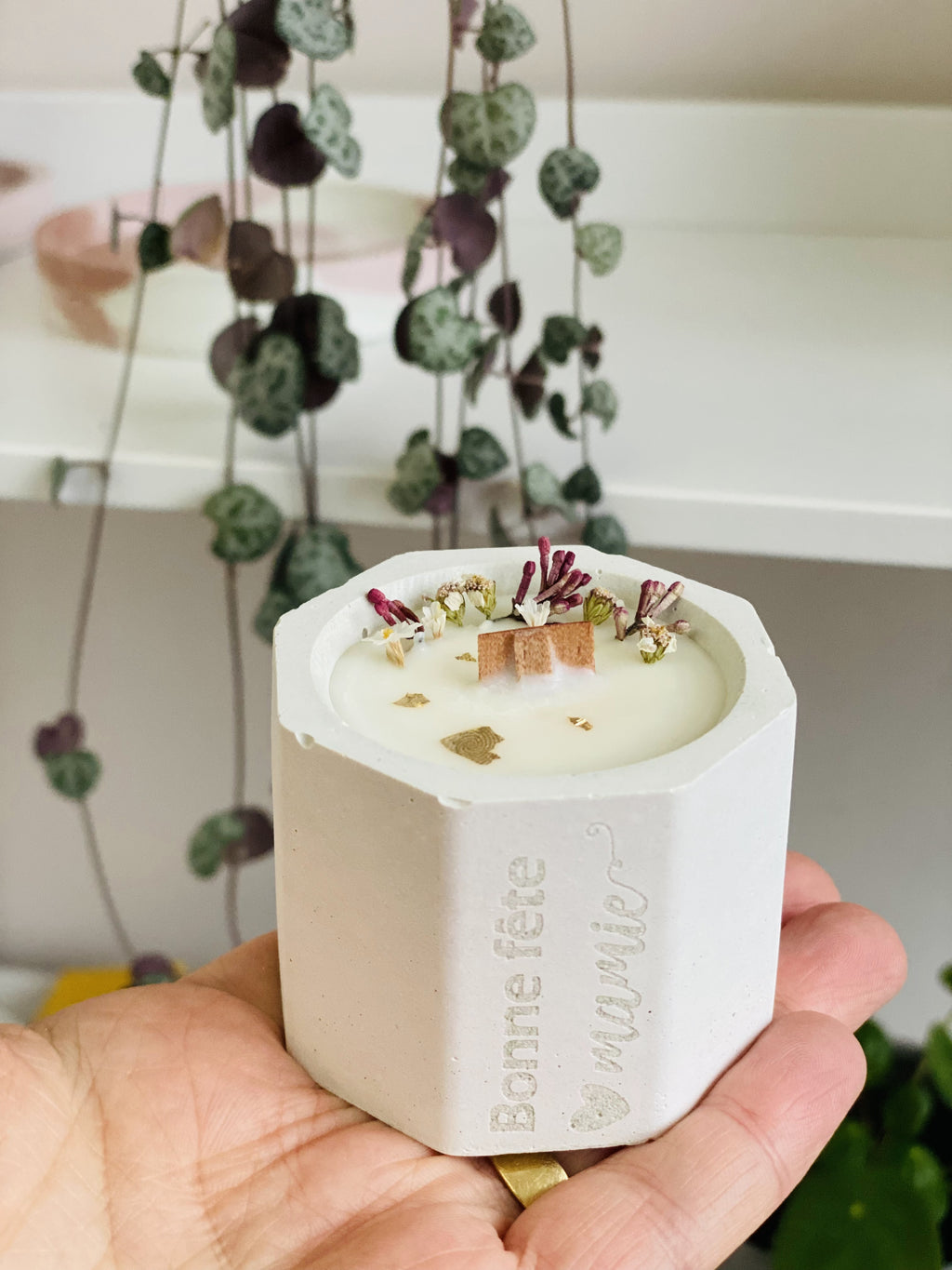 Bougie en béton blanc tenue en main avec fleurs roses et gravure 'Bonne fête mamie'