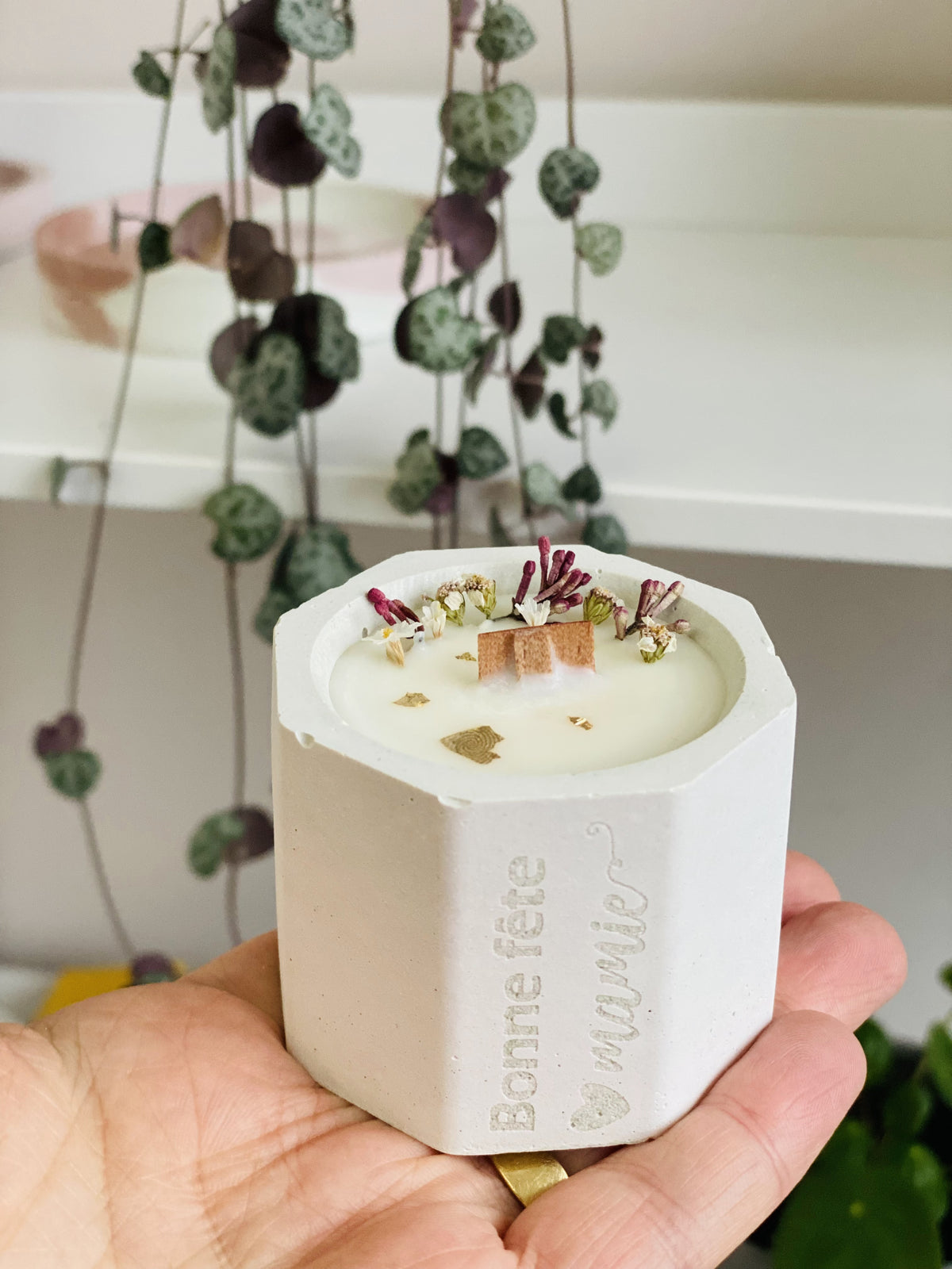 Bougie en béton blanc tenue en main avec fleurs roses et gravure 'Bonne fête mamie'