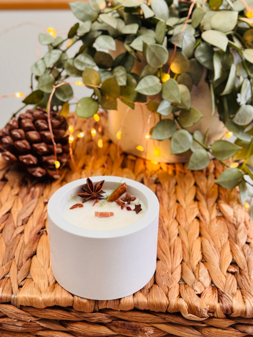 Bougie ronde dans un contenant en béton, décorée d’anis étoilé et de bâtons de cannelle.
