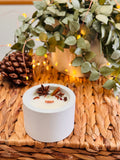 Bougie ronde dans un contenant en béton, décorée d’anis étoilé et de bâtons de cannelle.