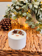 Bougie ronde dans un contenant en béton, décorée d’anis étoilé et de bâtons de cannelle.