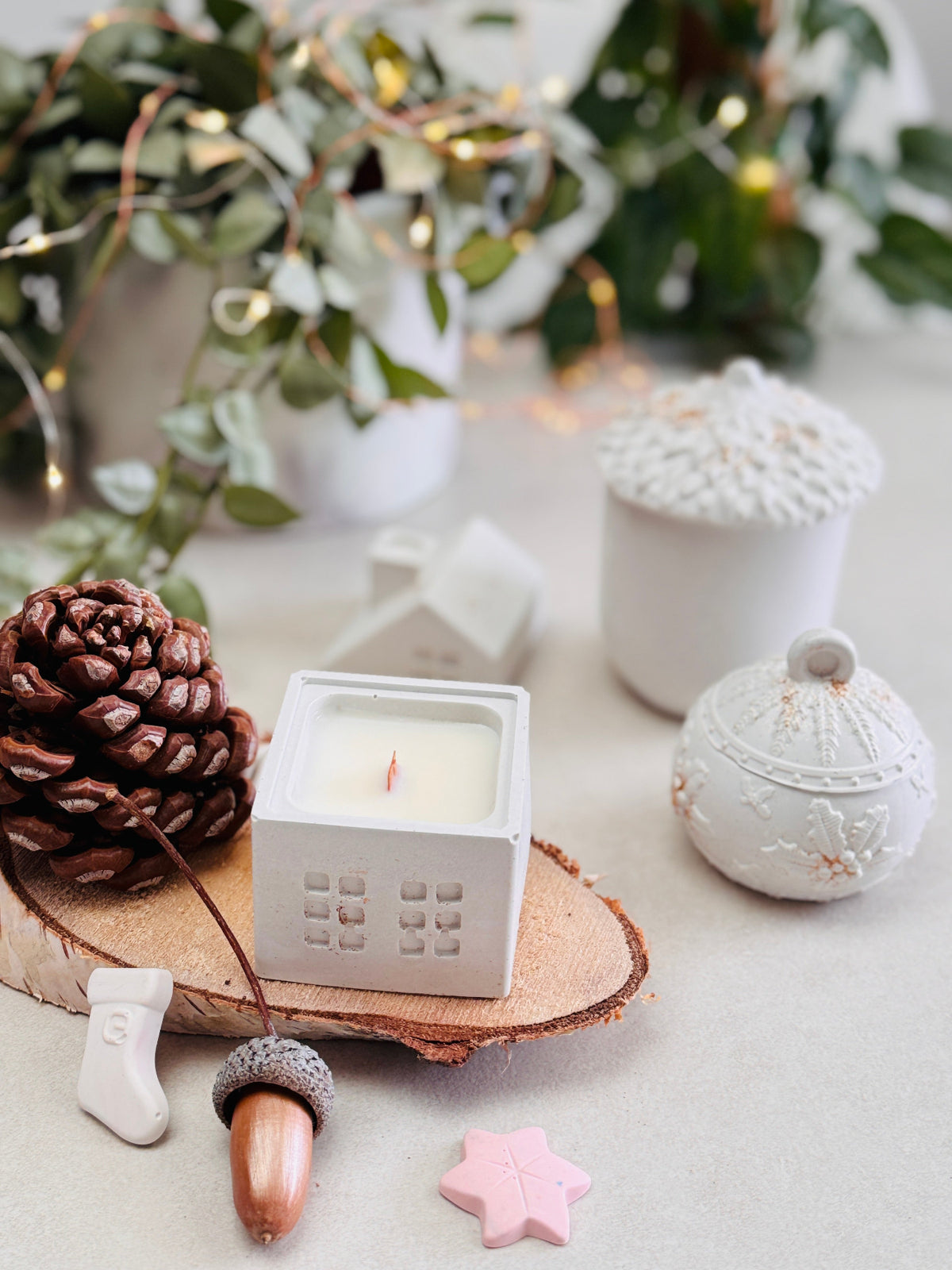 Bougies blanches avec maison, boule de sapin et gland dans une composition festive de Noël