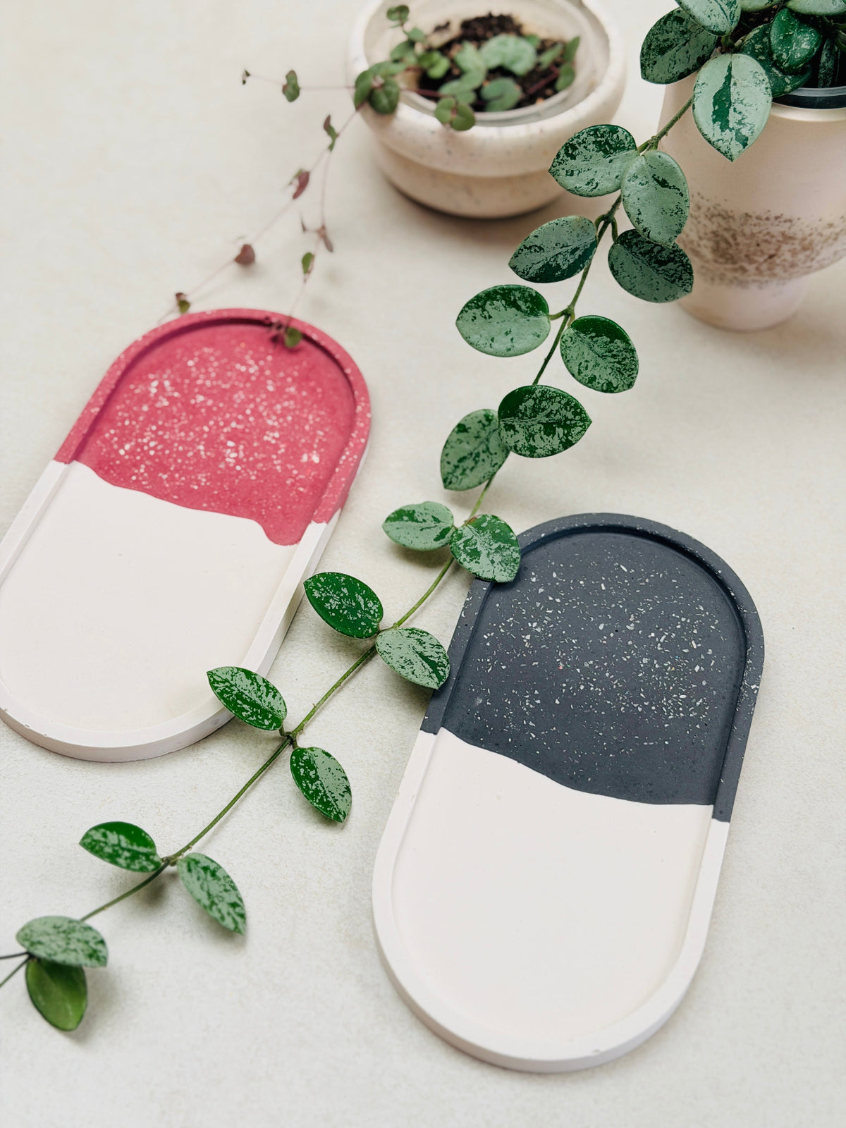 Deux plateaux ovales bicolores, bordeaux et blanc ou noir et blanc, à effet terrazzo, entourés de plantes