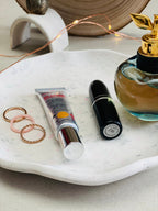 Gros plan sur un plateau en Jesmonite terrazzo gris et rose avec quelques bagues, parfum et maquillage