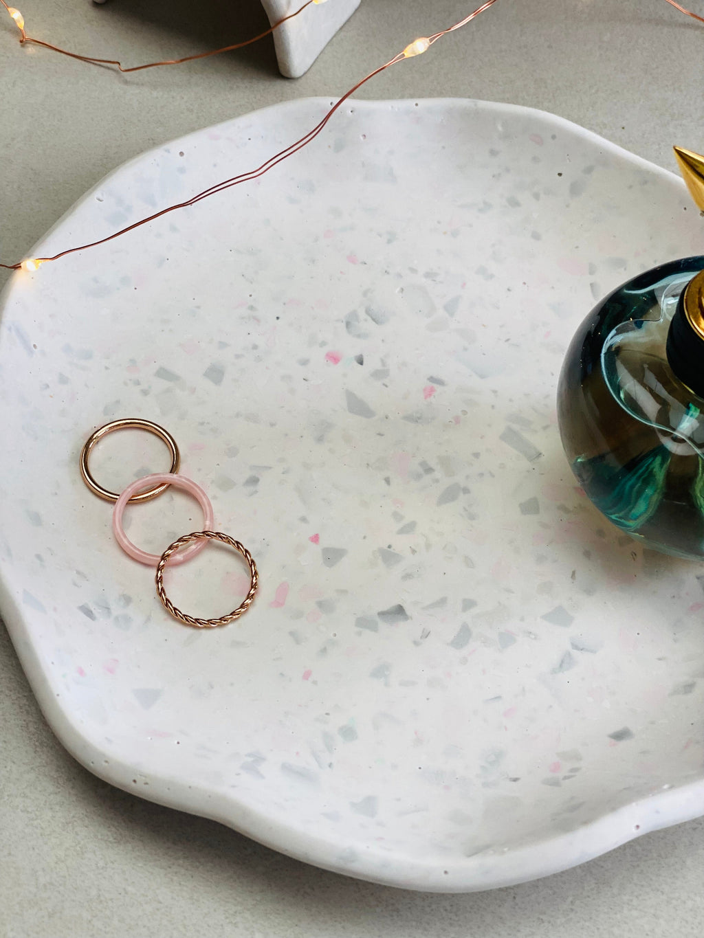 Gros plan sur un plateau en Jesmonite terrazzo gris et rose avec quelques bagues et un parfum