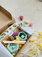 Kit DIY pour fabriquer des bougies florales, avec deux bougeoirs verts en béton, cire de soja, mèches en coton, fleurs séchées et accessoires de fabrication.
