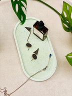 Plateau ovale en Jesmonite vert clair moucheté effet terrazzo, avec quelques bijoux et un produit de soin.