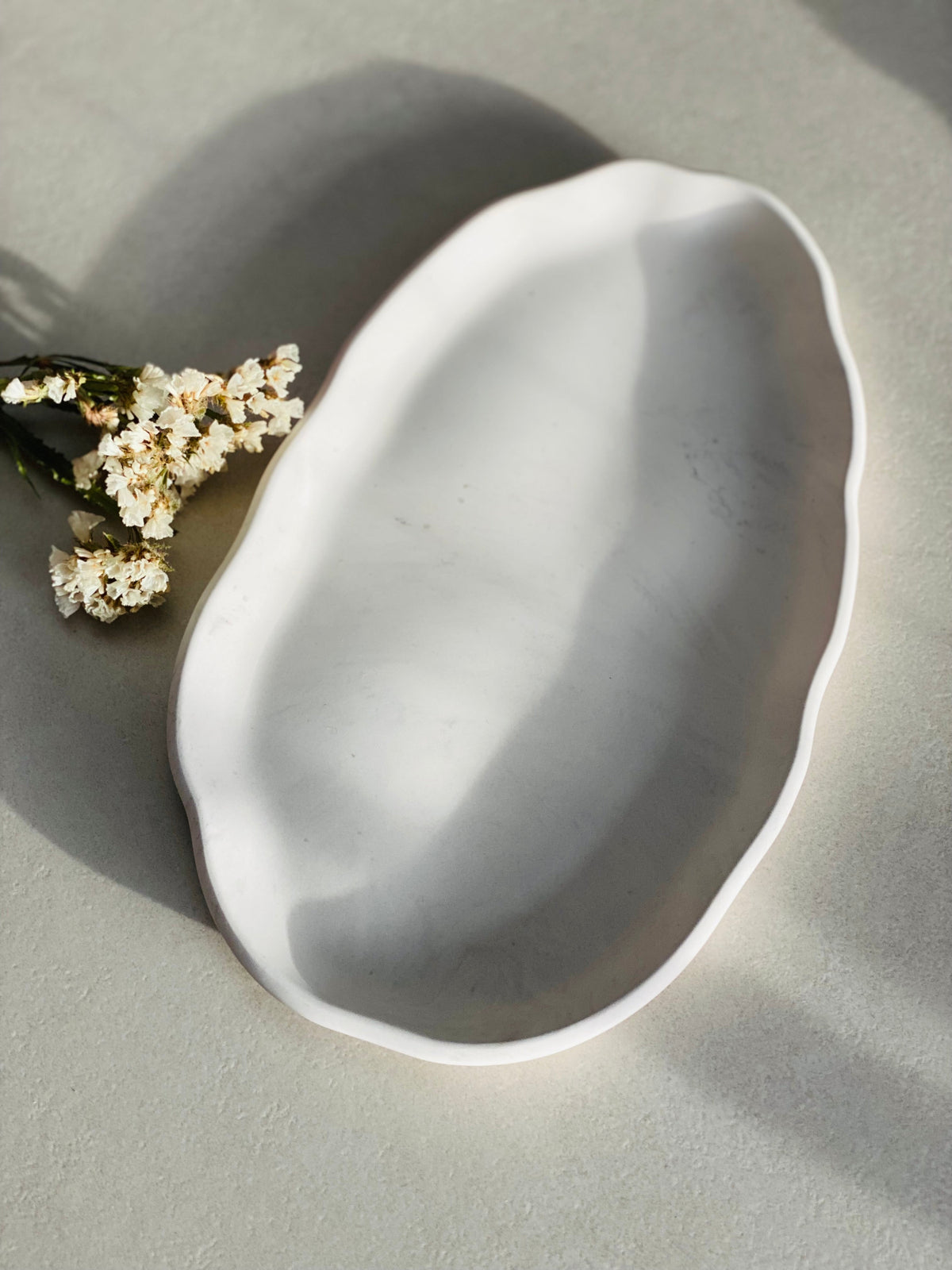 Plateau ovale irrégulier en Jesmonite marbrée gris et blanc posé sur une table à cote des fleurs séchées 