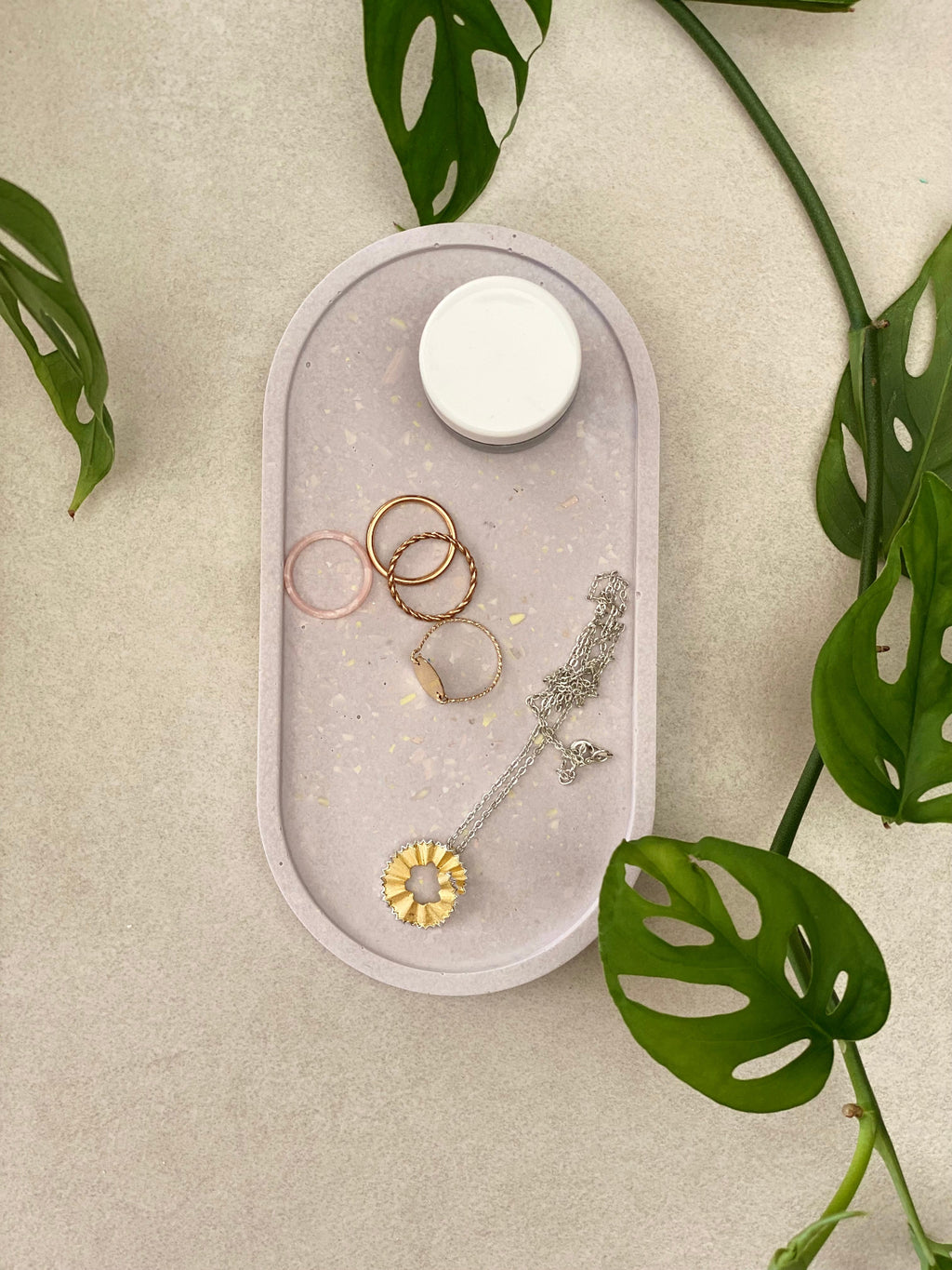 Plateau ovale rangement de bijoux en Jesmonite lilas moucheté effet terrazzo, avec quelques bijoux et un produit de soin.