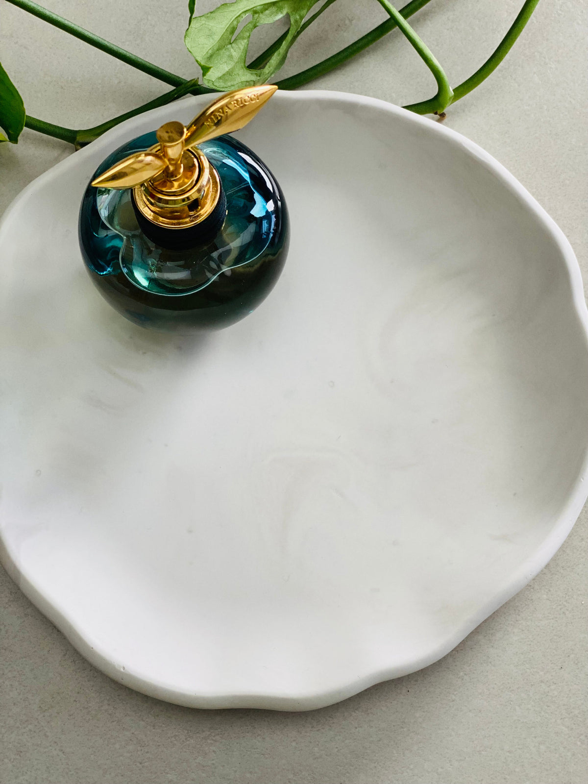 Plateau rond en Jesmonite blanc avec de légers effets marbrés gris, avec un parfum posé dessus