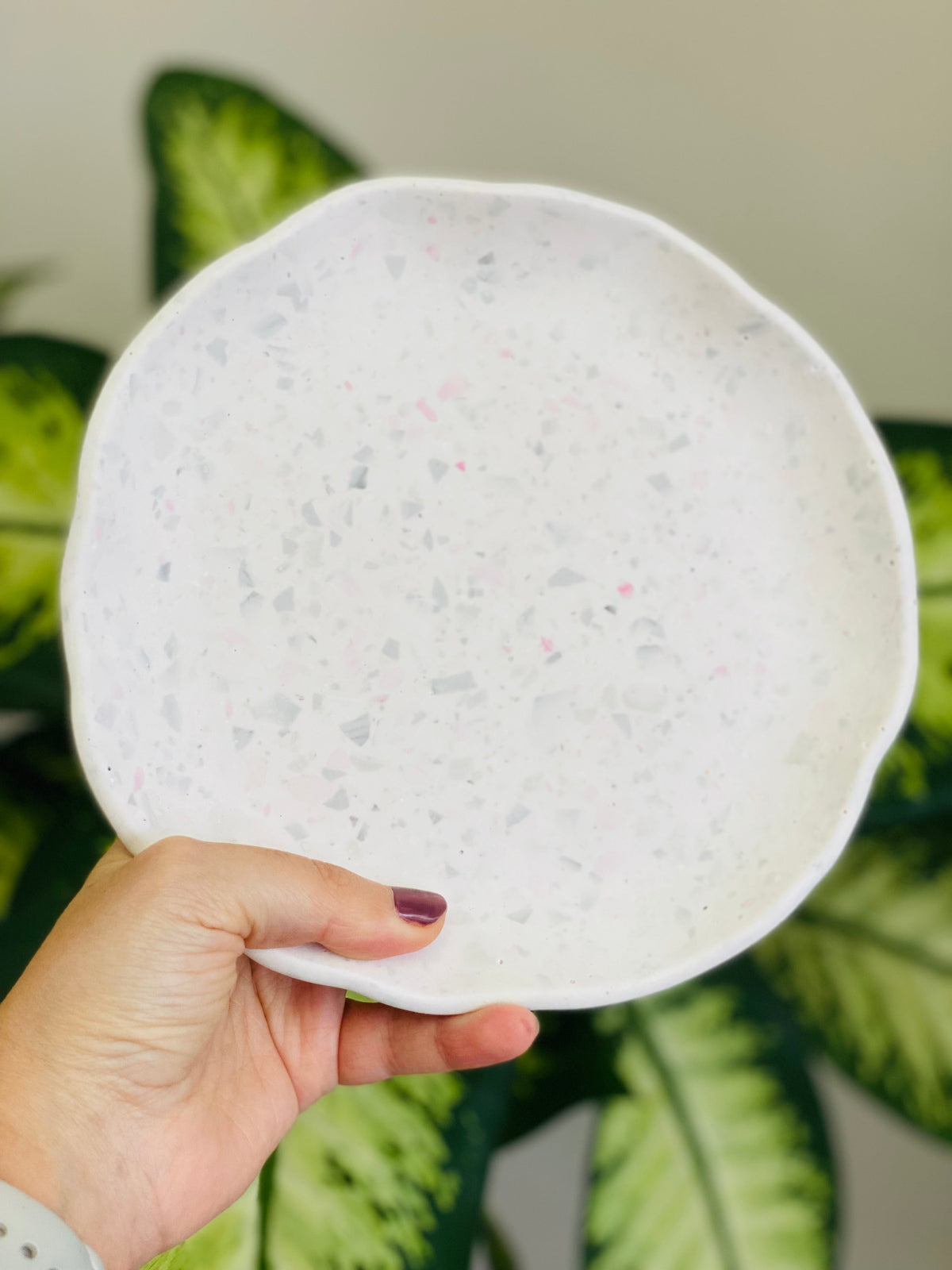 Plateau rond en Jesmonite terrazzo gris et rose tenu dans une main