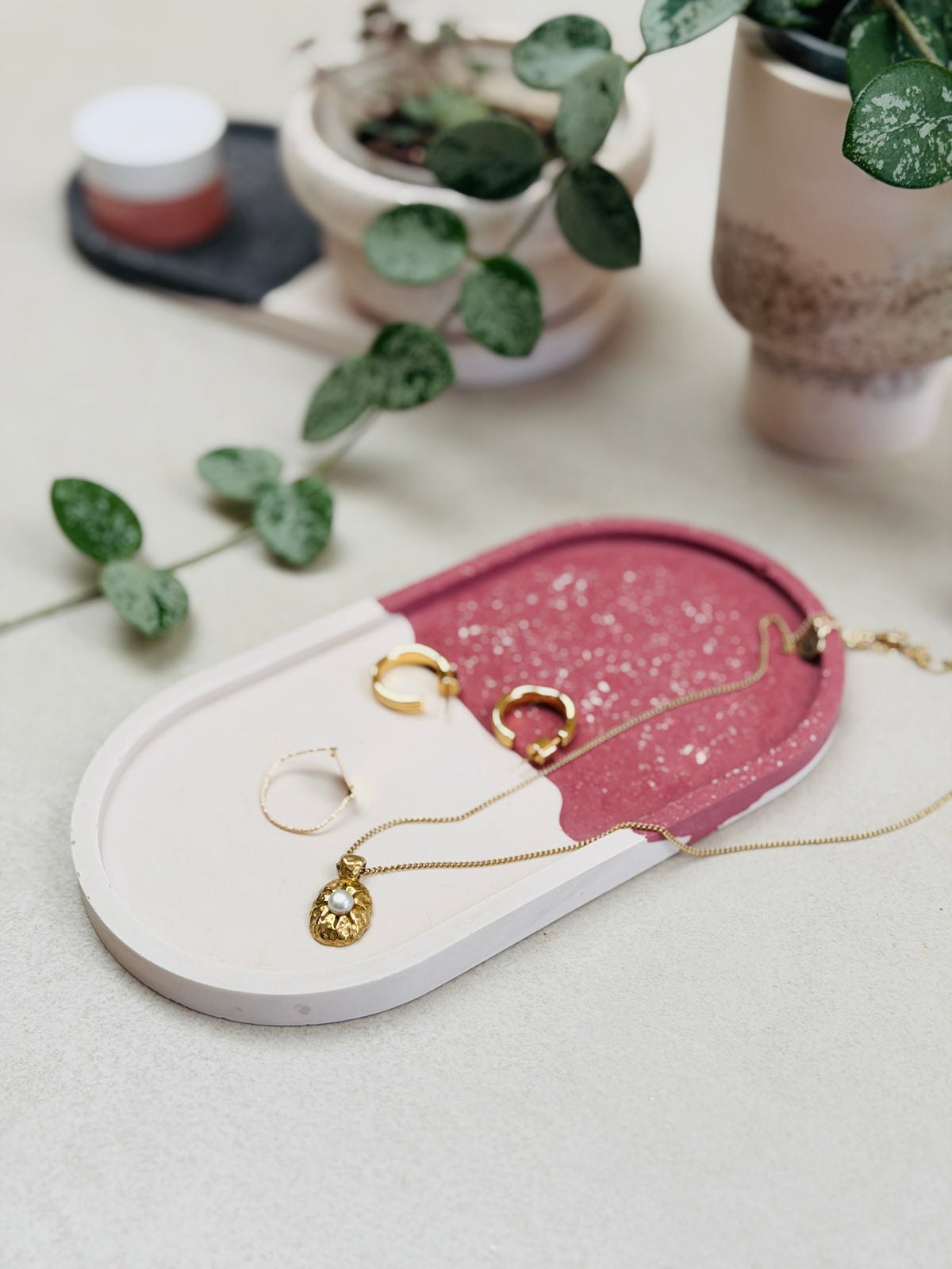 Plateau vide-poche ovale bordeaux et blanc à effet terrazzo, avec un collier, des boucles d’oreilles et une bague.