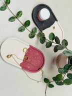 Plateaux jesmonite ovales à effet terrazzo bordeaux et noir sur fond blanc, utilisés pour ranger des bijoux et un petit pot de crème 