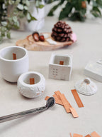 Bougeoirs blancs prêts à être coulés, avec leurs mèches en bois, dans une ambiance de Noël