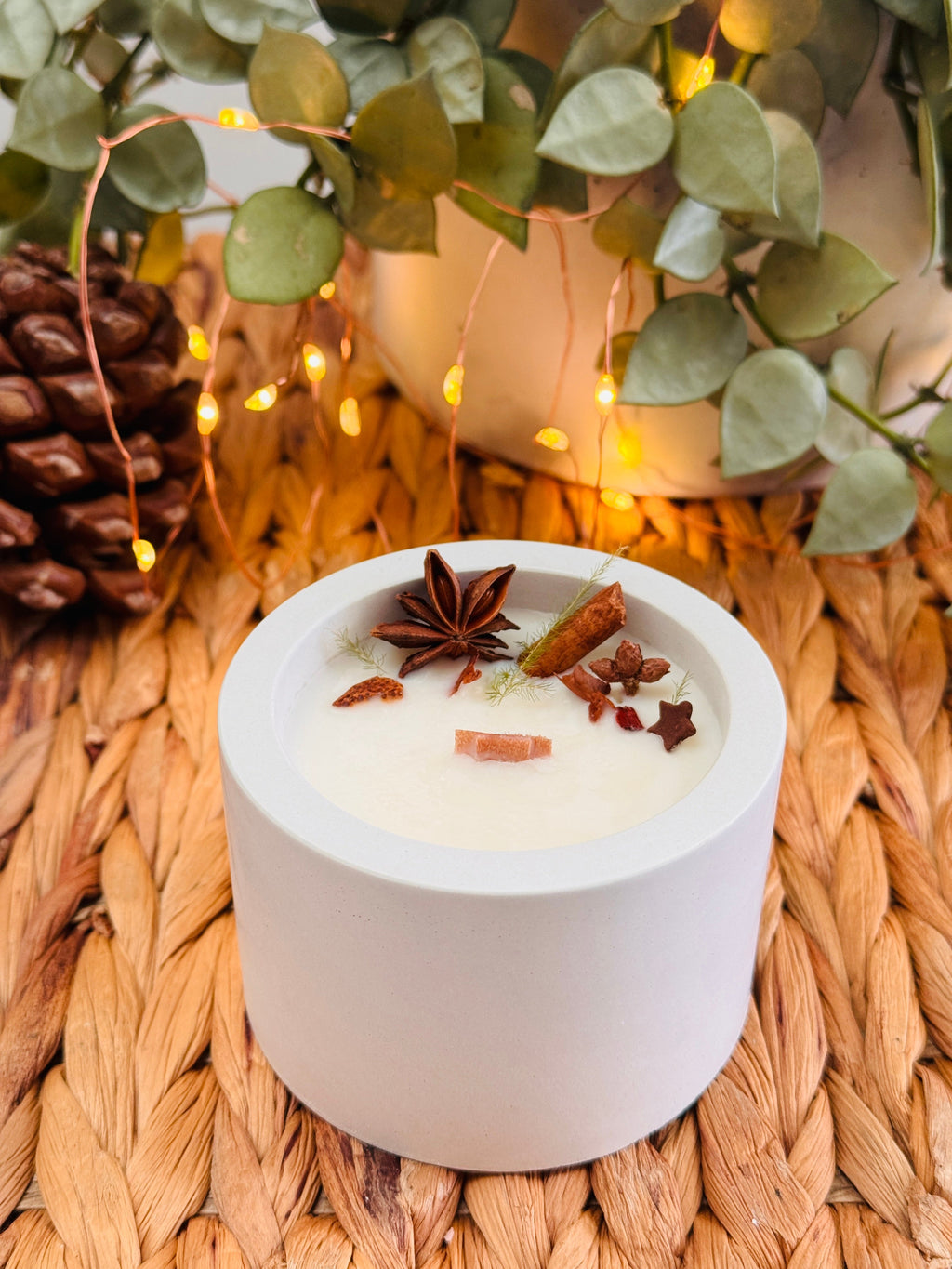 Bougie ronde dans un contenant en béton, décorée d’anis étoilé et de bâtons de cannelle.