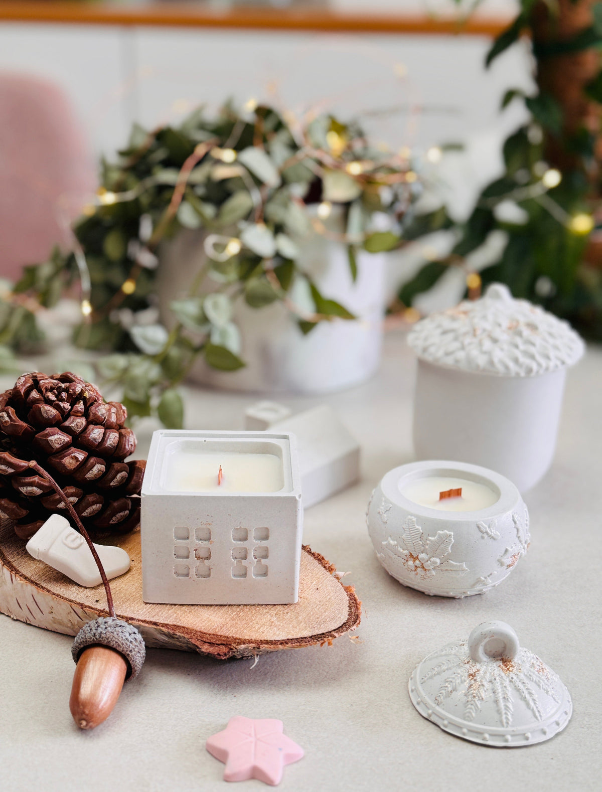 Bougies blanches avec maison, boule de sapin et gland dans une composition festive de Noël