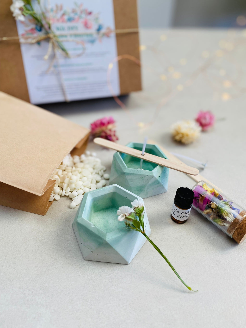 Kit DIY pour fabriquer des bougies florales, avec deux bougeoirs verts en béton, cire de soja, mèches en coton, fleurs séchées et accessoires de fabrication.
