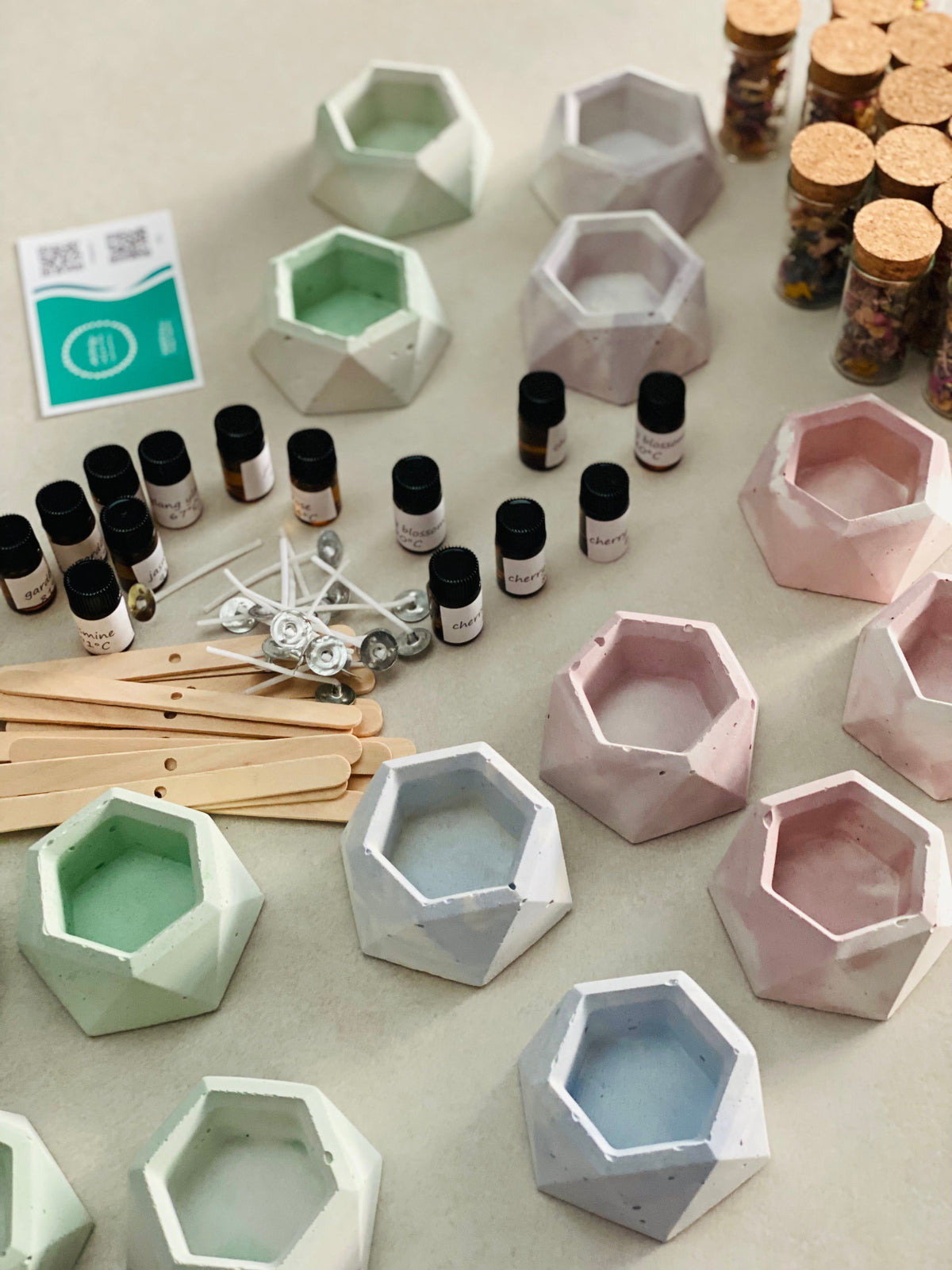 Plusieurs bougeoirs en béton de différentes couleurs, accompagnés de flacons de fleurs séchées, de mèches en coton, de supports de mèches et de flacons de parfum.