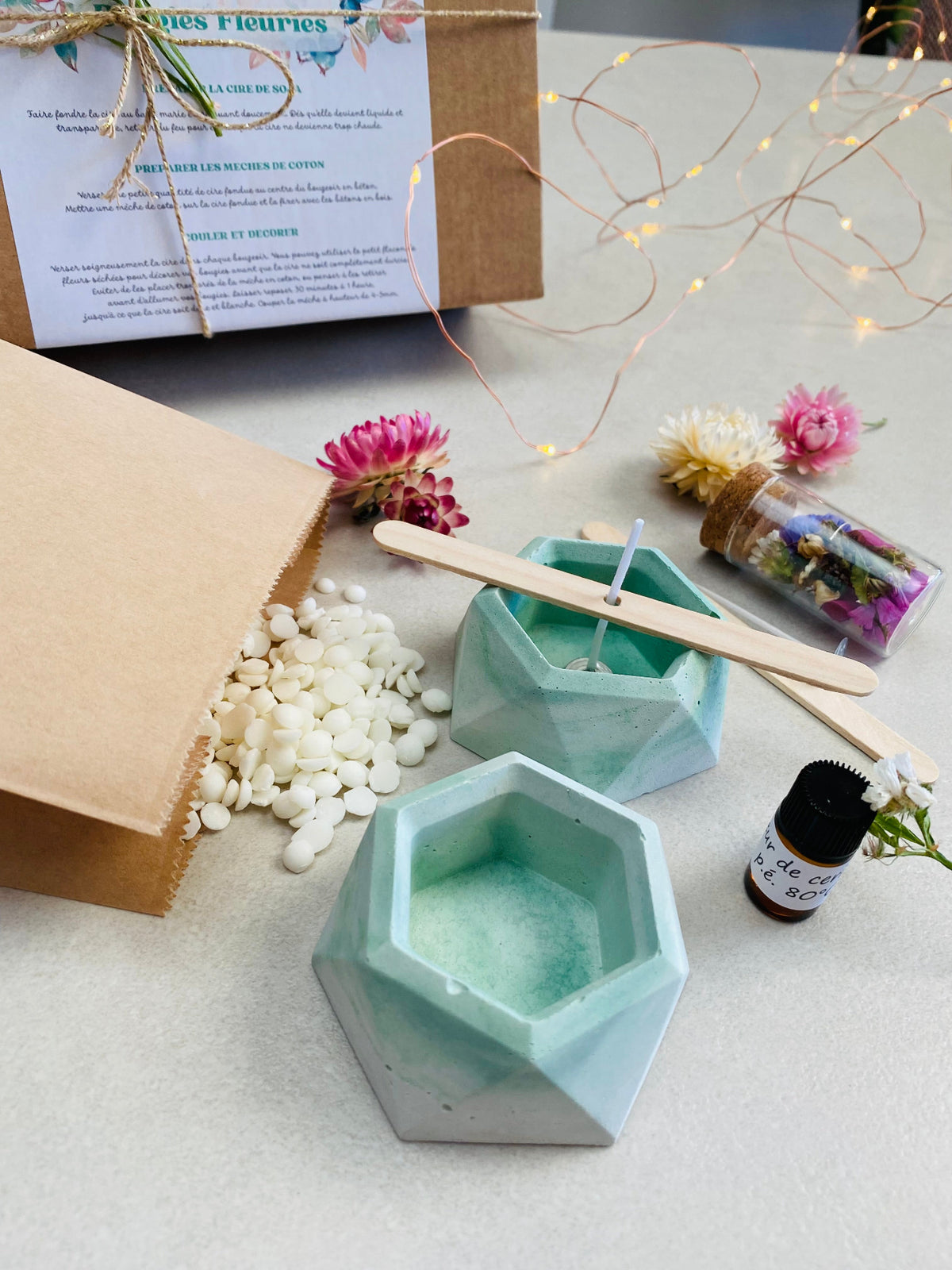 Présentation du kit DIY pour fabriquer des bougies florales, avec deux bougeoirs verts en béton, cire de soja, mèches en coton, fleurs séchées et accessoires de fabrication.
