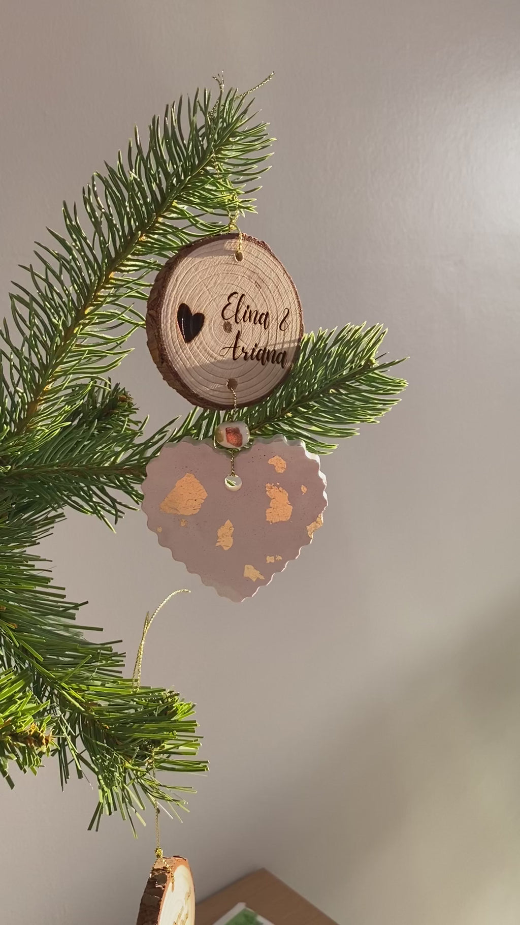 Vidéo de création d’une décoration de Noël personnalisée avec gravure sur bois et cœur artisanal parsemé de feuilles d’or, suspendu à une branche de sapin.