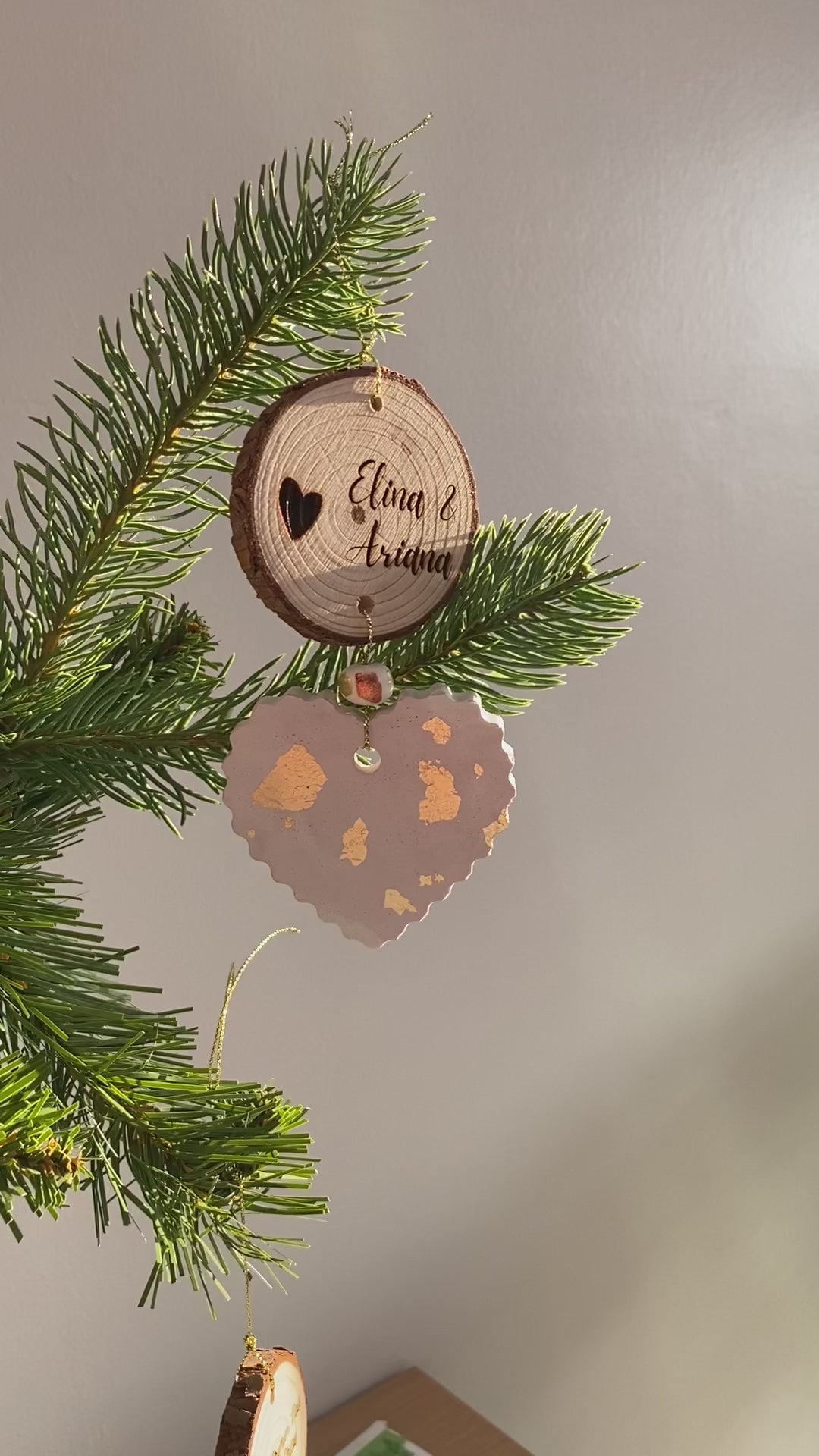 Vidéo de création d’une décoration de Noël personnalisée avec gravure sur bois et cœur artisanal parsemé de feuilles d’or, suspendu à une branche de sapin.