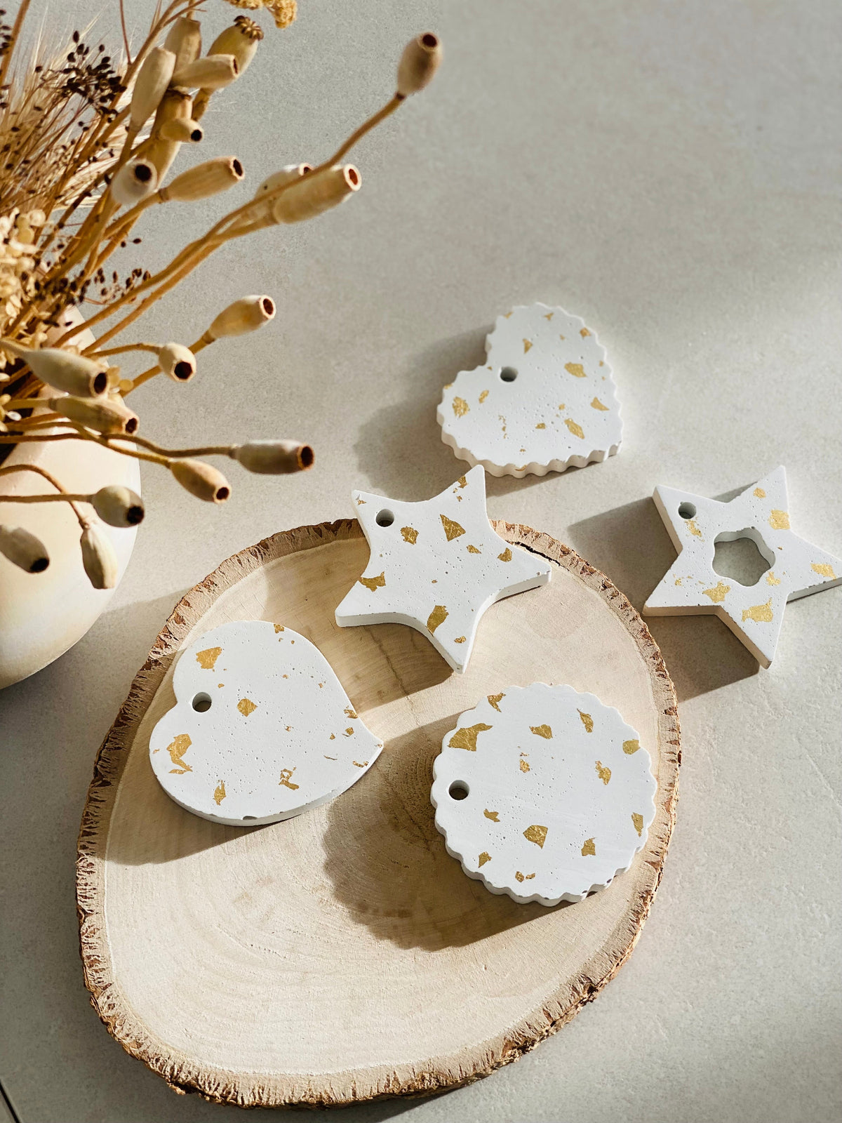 Décorations de sapin en béton et feuilles d’or présentées sur un rondin de bois sur une table